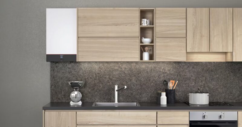 A white Viessmann Vitodens combi boiler mounted on a grey wall above a modern kitchen worktop with sink, scales and utensils