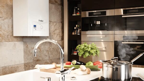 A white Vaillant ecoTEC pro wall-hung boiler installed in a modern kitchen above a sink with vegetables and a steaming pot on the hob
