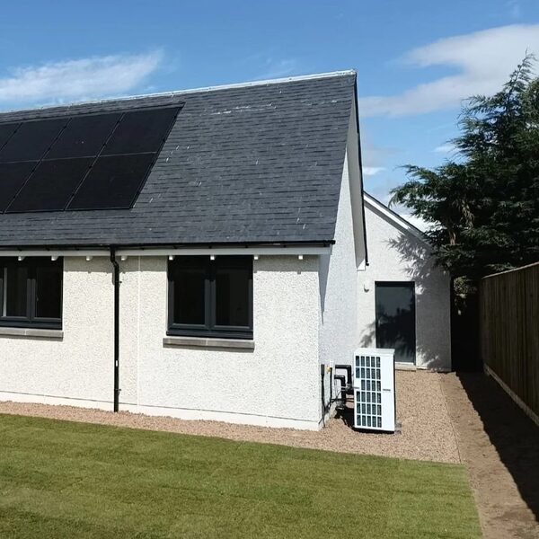 An air source heat pump unit installed outside a white rendered bungalow with solar panels on the slate roof