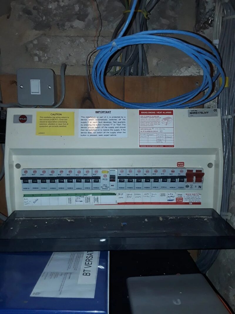 A Wylex consumer unit with MCBs and RCD mounted on a rough wall with coiled blue cable and a light switch above