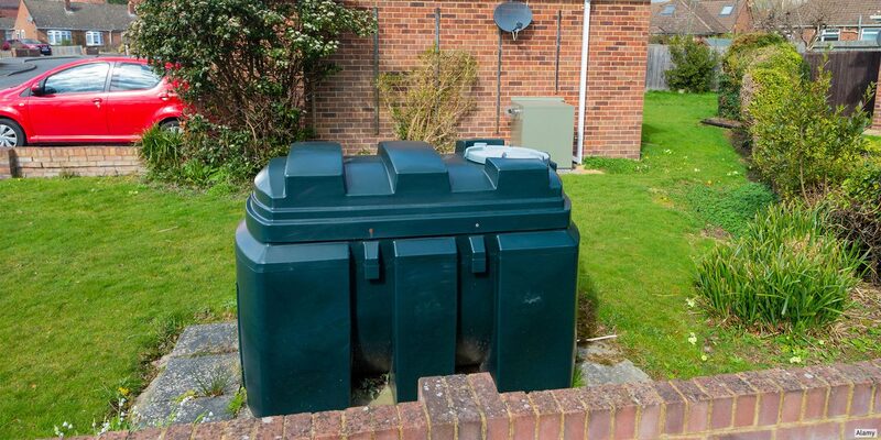 A dark green plastic heating oil tank installed on a slab in a suburban back garden beside a brick house