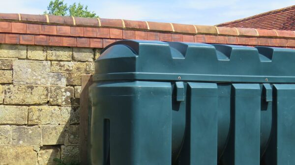 A green plastic heating oil tank installed against a stone wall with a tiled roof behind it