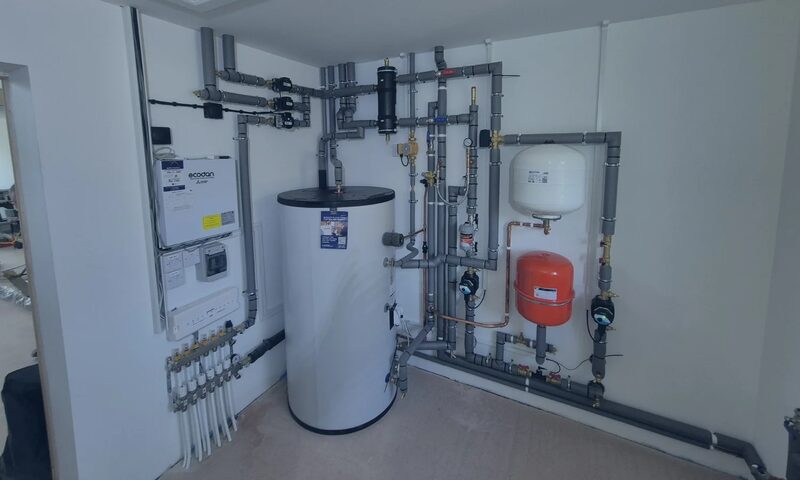 A heat pump heating system installation with a cylinder, pipework, expansion vessels and an Ecofen control unit in a utility room