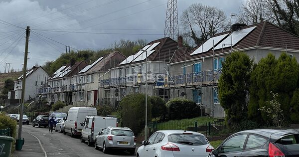 A row of UK houses with rooftop solar panels and scaffolding during a retrofit installation on a residential street