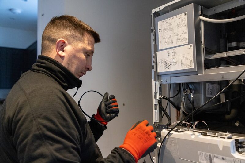 An engineer in orange gloves installing an indoor heat pump unit inside a home