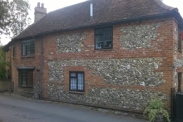 An old brick and flint cottage with dark timber casement windows, shown as a before photo