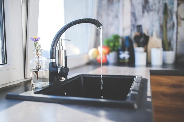 A black kitchen mixer tap running water into a black sink in a bright kitchen