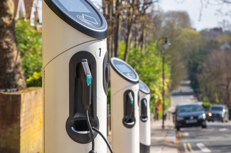 A row of cream-coloured public electric vehicle charge points with cables on a residential UK street