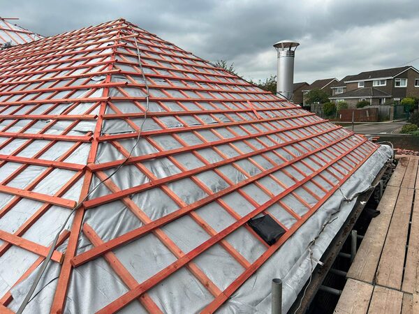 A house roof under construction with silver multifoil insulation fitted beneath red wooden battens