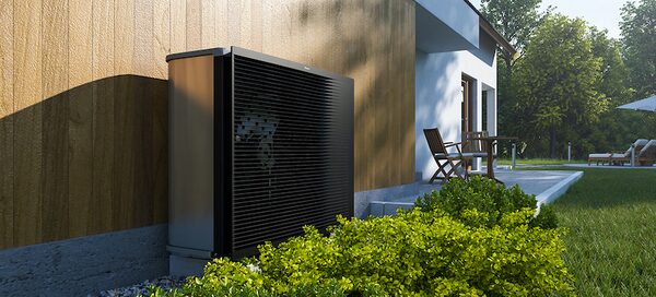 A modern black air source heat pump unit installed outside a timber-clad house beside a patio and garden