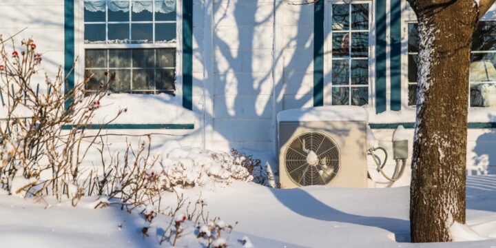 An air source heat pump unit installed outside a snow-covered house in winter