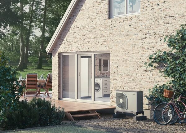 An air source heat pump unit installed outside a brick house next to a patio and bicycles
