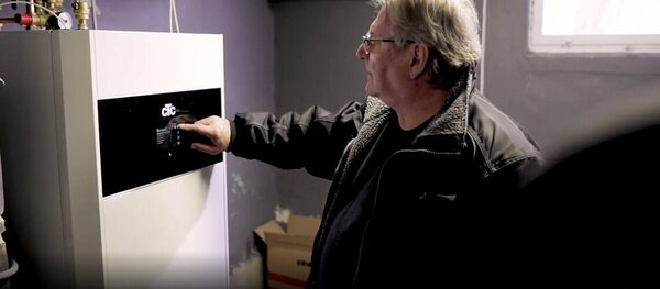 A man pressing the control panel of a CTC indoor heat pump unit installed in a utility room