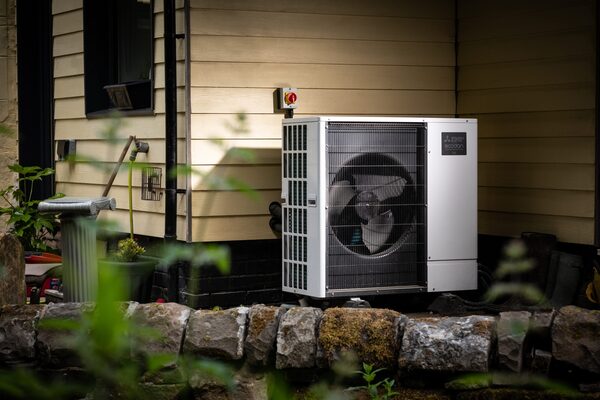 An air source heat pump unit installed outside a house beside a stone wall