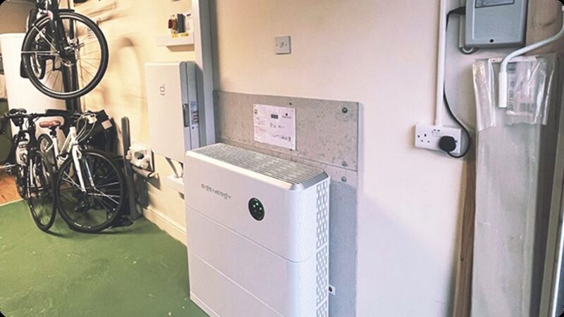 A Sigenergy home battery installed on a garage wall next to an inverter, with bicycles parked nearby