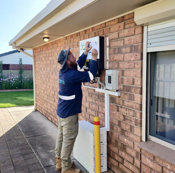 A technician installing a Growatt solar inverter and battery on the exterior brick wall of a house