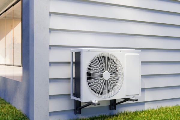 A white air source heat pump unit mounted on the outside wall of a house