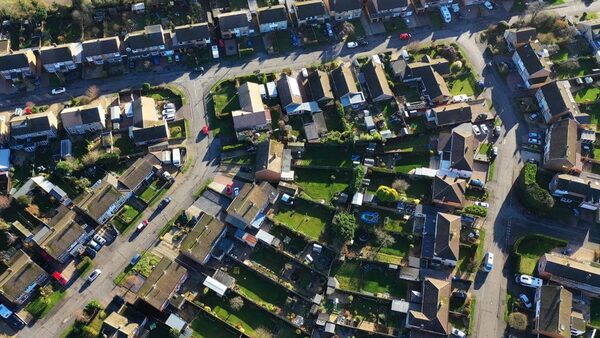 An aerial view of a UK suburban housing estate with rows of houses, gardens and parked cars