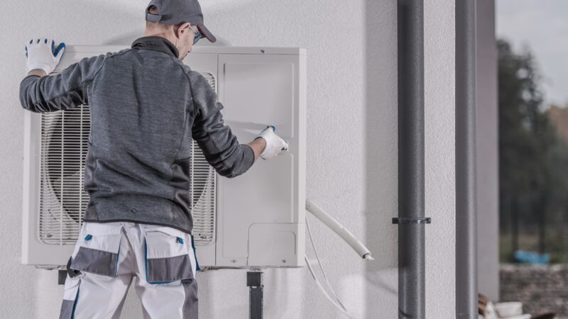 An engineer in workwear installing an air source heat pump outdoor unit on an exterior wall