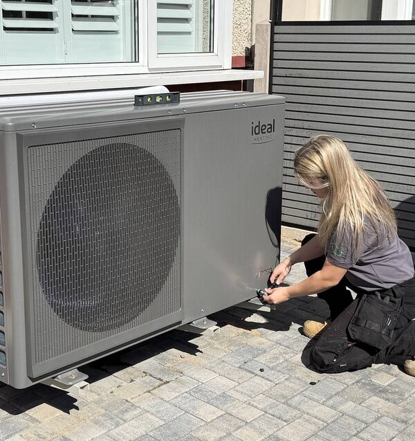 A technician installing an Ideal Heating air source heat pump outside a house