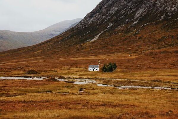 A lone white cottage in a remote Scottish glen with autumn moorland and mountains