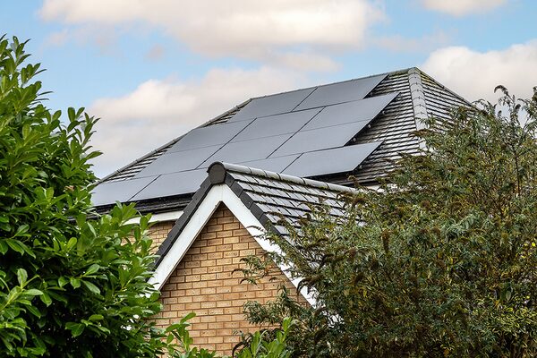 Solar panels installed on the tiled roof of a brick house surrounded by trees