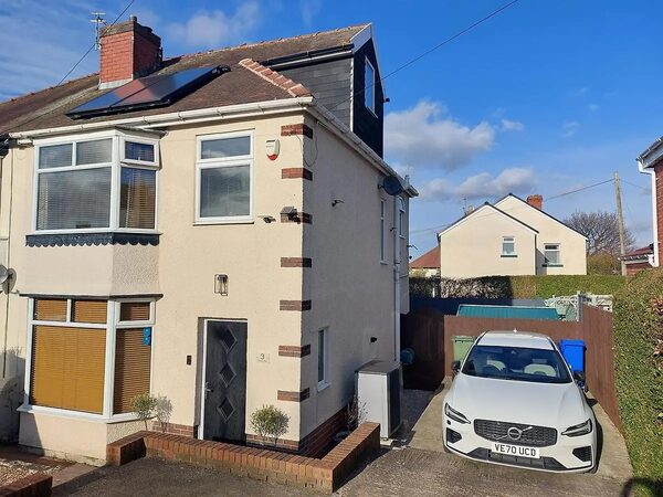 A semi-detached house with solar panels on the roof and an air source heat pump unit beside the driveway, with a white Volvo parked outside