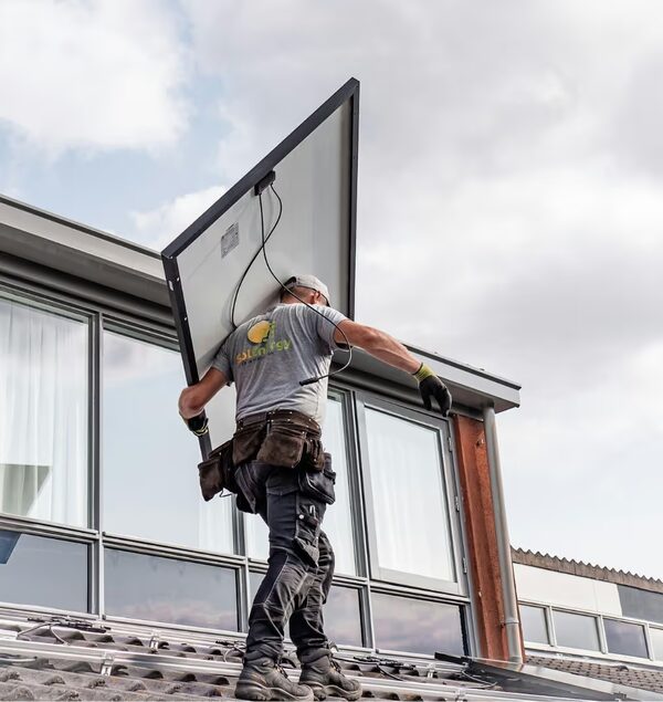 An installer carrying a solar panel up a tiled roof during installation