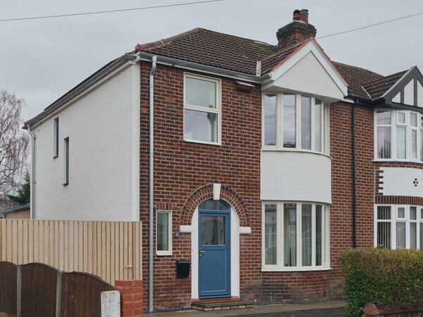 A retrofitted brick semi-detached house with white external insulation and a blue front door under an overcast sky