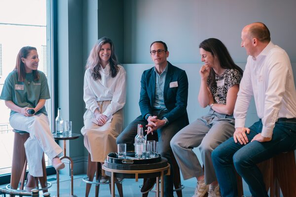 Five people in name badges sitting on stools in a panel discussion at an indoor event