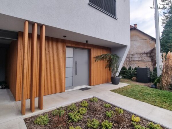 Exterior of a modern low-energy house with timber cladding and a heat pump unit beside the entrance