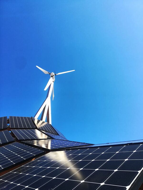 Solar panels on a roof with a small white wind turbine against a clear blue sky