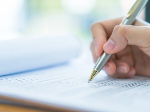 A hand holding a pen filling in a paper form on a clipboard
