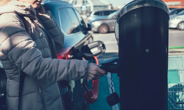 A woman plugging a charging cable into a public electric vehicle charge point in a car park