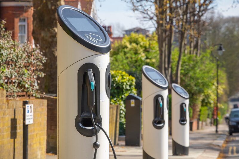 A row of white public EV charge points installed along a residential street pavement