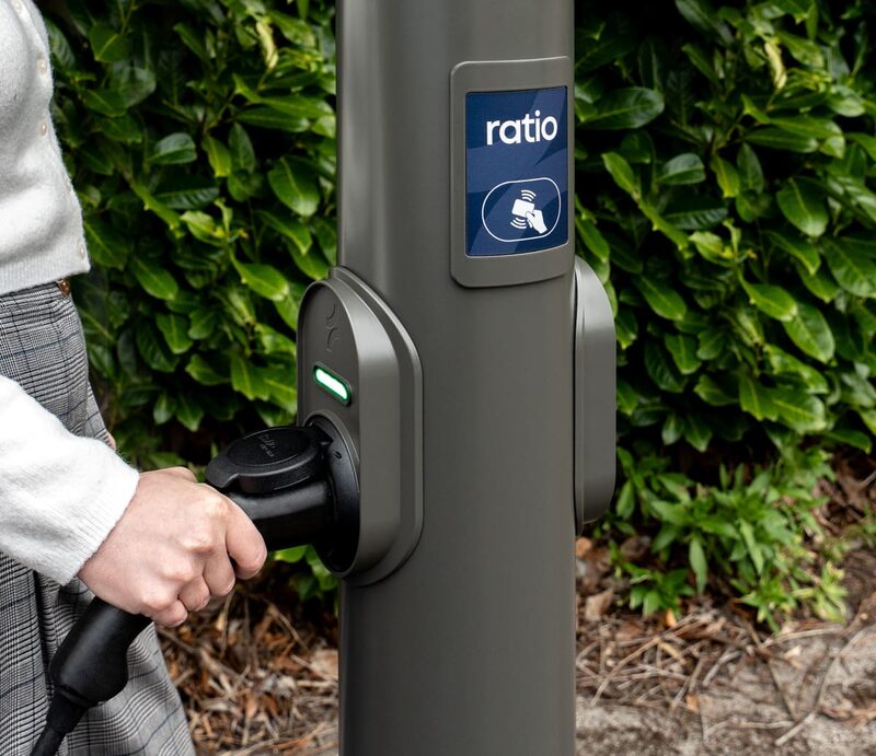 A person plugging a charging cable into a grey Ratio public EV charge post with a contactless payment panel