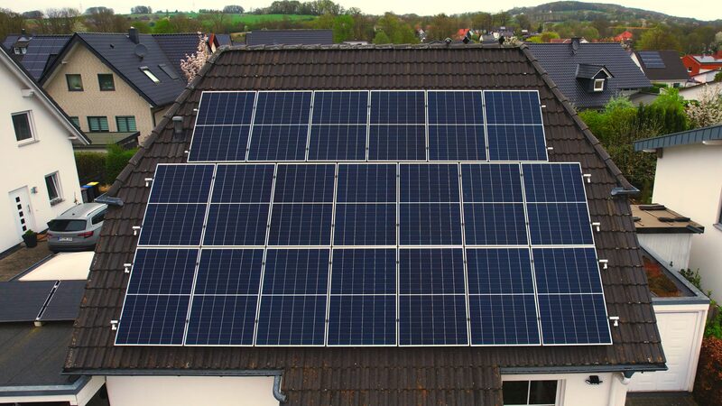 A large array of rooftop solar panels installed on the tiled roof of a house in a residential neighbourhood