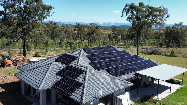 Aerial view of a large tiled-roof house with black solar panels installed across the roof in a rural setting