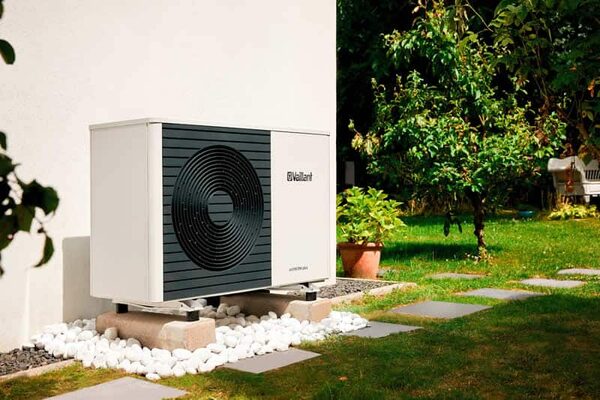 A Vaillant air source heat pump installed outside a house on a gravel bed beside a garden path