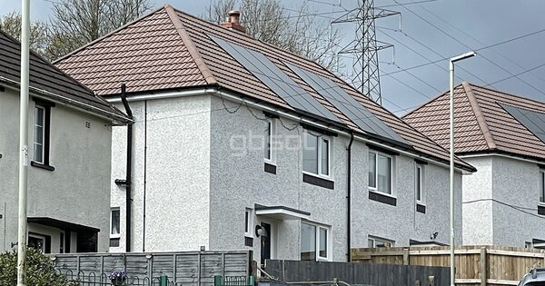A semi-detached house with solar panels on its tiled roof, with a neighbouring house also fitted with panels