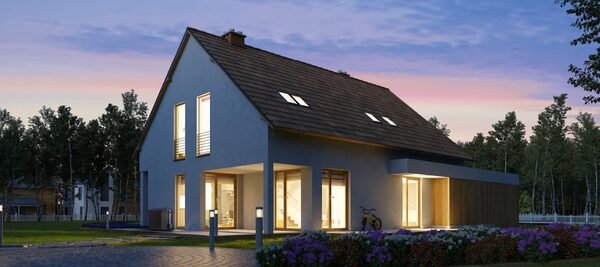 A modern two-storey house at dusk with lit windows, a garden and an air conditioning heat pump unit beside the wall