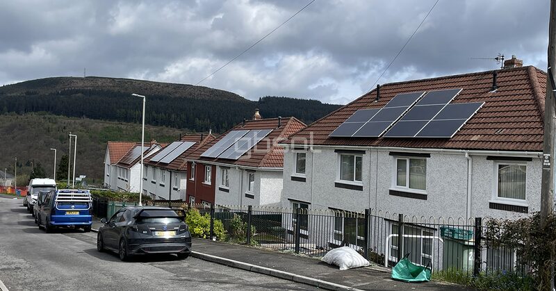 A row of terraced houses with rooftop solar panels on a Welsh hillside street