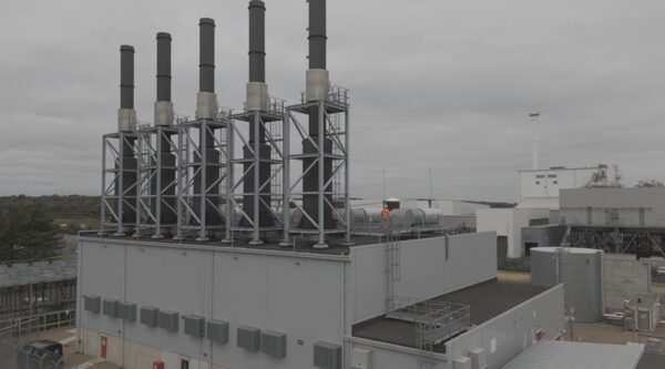 An industrial gas-fired power station with tall exhaust stacks and steel framework under an overcast sky