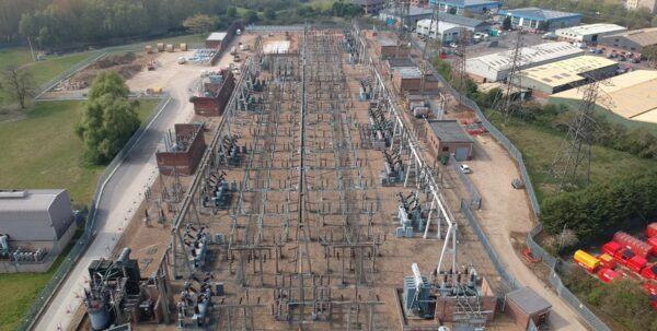 An aerial view of a large electricity substation with switchgear, transformers and pylons surrounded by industrial buildings