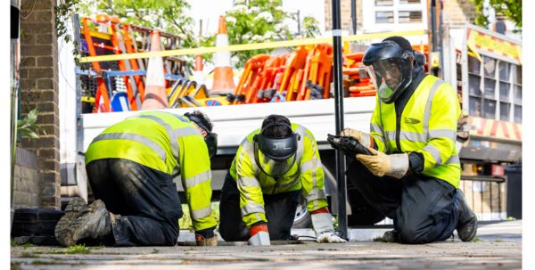 Three UK Power Networks engineers in high-visibility jackets and face shields working on underground electricity cables on a residential street