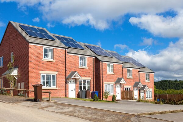A row of new red-brick UK houses with solar panels installed on their roofs under a blue sky