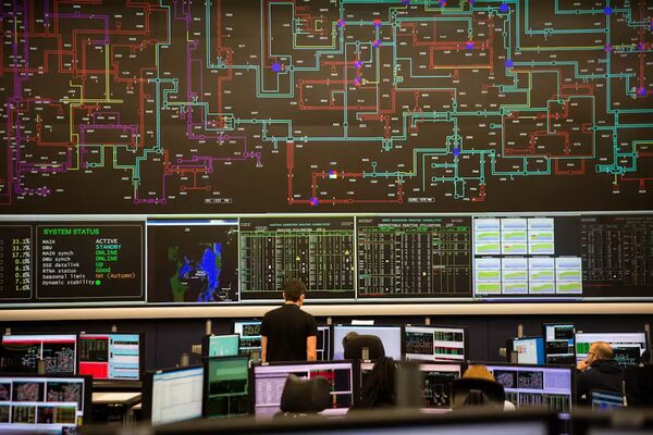 A national grid control room with a large wall of network status screens and operators at monitoring desks