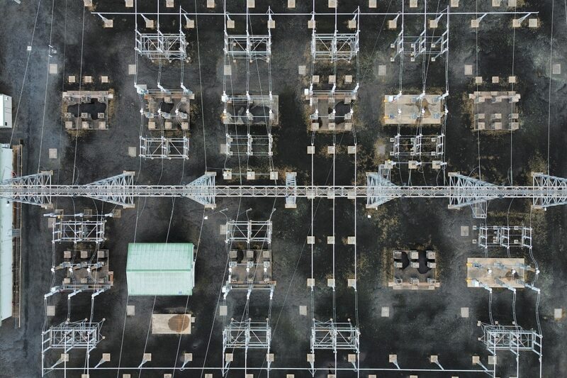 Aerial view of an electrical substation with switchgear, pylons and a small green building