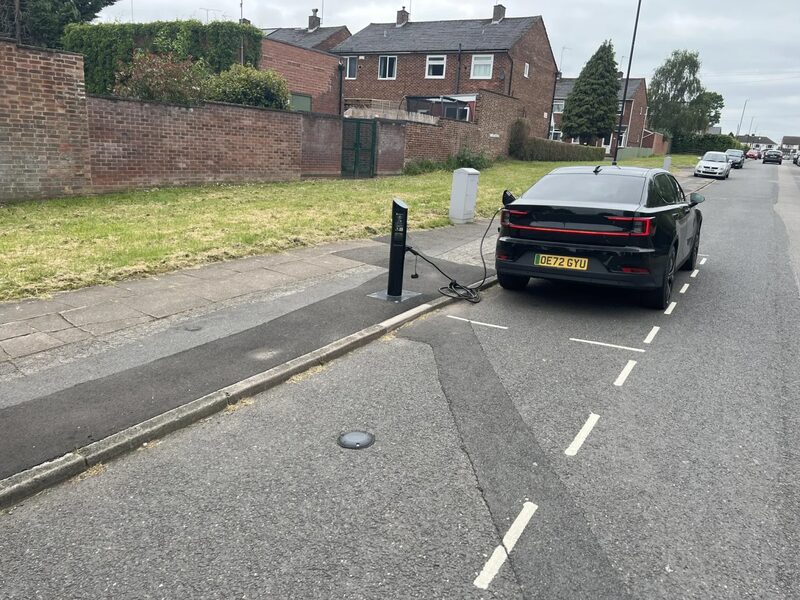 A black electric car charging from a kerbside EV charge point on a UK residential street