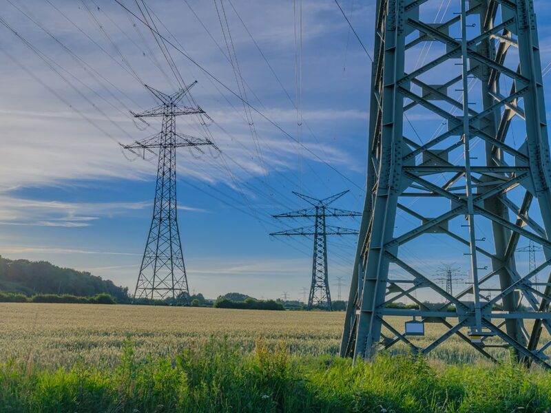 High-voltage electricity transmission pylons and power lines over a green farmland field under a blue sky
